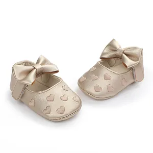 Detaillierte Ansicht goldener Baby-Prinzessinenschuhe mit Schleifen und Herzmustern.