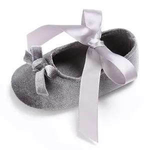 Détail d'une chaussure de bébé en velours gris avec un grand nœud en ruban de satin