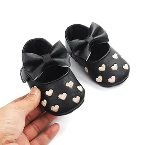 Nahaufnahme von Baby-Prinzessin-Schuhen mit Herzstickerei und schwarzer Schleife.