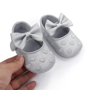 Nahaufnahme von silbernen Baby-Lernlaufschuhen mit Herzstickerei und großer Schleife.