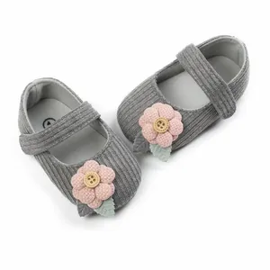 Nahaufnahme von grauen Cord-Babyschuhen für Mädchen mit rosa Blumenapplikation