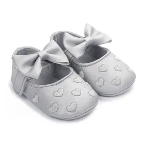 Makro-Detail von silbernen Baby-Lernlaufschuhen mit Schleife und Herzstickerei.