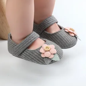 Detailansicht grauer Strick-Babyschuhe für Mädchen mit rosa Blume und Holzknopf.