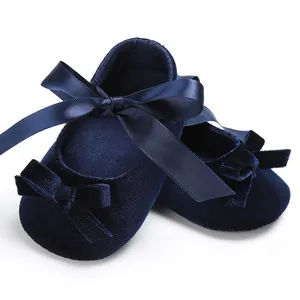 Vue détaillée de chaussures bébé en velours bleu marine avec ruban satin et nœuds.