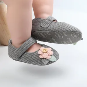 Nahaufnahme von grauen gestrickten Babyschuhen mit rosa Blume und rutschfester Sohle.