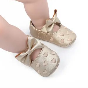 Detailansicht goldener Baby-Prinzessinenschuhe mit Schleife und Herzmuster-Stickerei