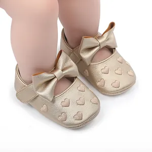 Nahaufnahme von goldenen Baby-Prinzessin-Schuhen mit Schleife und Herzstickerei.