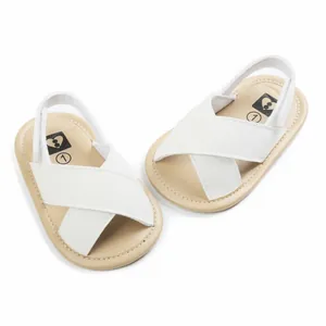 Close-up view of white cross-strap baby pre-walker sandals with soft tan soles