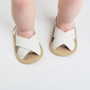 White criss-cross baby sandals with soft anti-slip soles shown on infant feet in detail