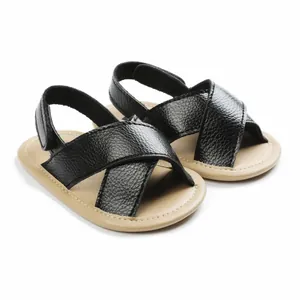 Close-up of black faux leather baby sandals with cross-straps and soft beige soles