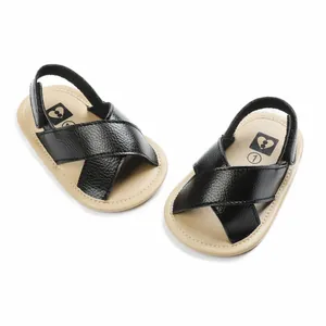 Close-up of black faux leather baby sandals with cross-strap design and tan soft soles