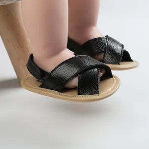 Close-up of black faux leather baby walking sandals with cross-straps and soft soles