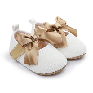 Detalle de zapatos de princesa de punto para bebé con lazos grandes de satén dorado.