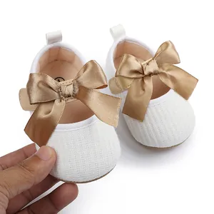 Primer plano de zapatos de princesa para bebé en blanco con un elegante lazo de raso dorado