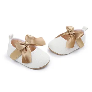 Detalle de zapatos de princesa blancos para bebé con un gran lazo de satén dorado