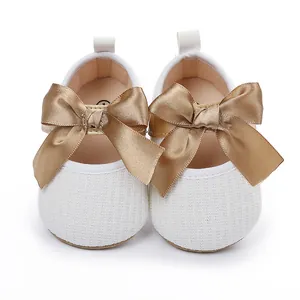 Vista frontal de zapatos de princesa para bebé en punto blanco con lazo de satén dorado