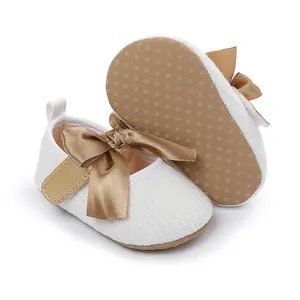Detalle de zapatos blancos de princesa para bebé con lazo dorado y suela antideslizante.