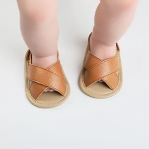 Close-up view of brown textured leather cross-strap infant sandals with soft non-slip soles