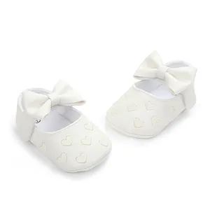 Close-up of white baby pre-walker shoes featuring heart embroidery and a bow strap