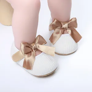 Primer plano de zapatos blancos de princesa para bebé con elegantes lazos de satén dorado