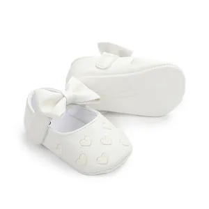 Close-up detail of white baby walking shoes with embroidered hearts and an elegant bow