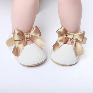 Primer plano de zapatos blancos de princesa para bebé con un gran lazo de satén dorado.