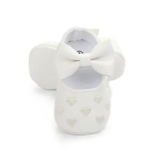 Close-up of white baby pre-walker shoes featuring a large bow and heart-shaped embroidery