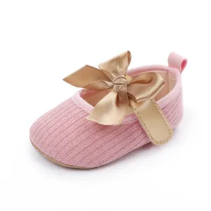Detalle de zapatos de punto rosa para bebé con un gran lazo de satén dorado