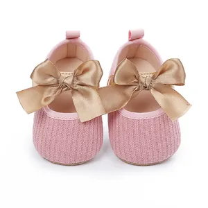 Detalle de zapatos de bebé de punto rosa con un gran lazo de satén dorado