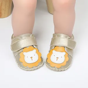 Zapatos de bebé dorados con parche de león amarillo y detalle de cierre de velcro.