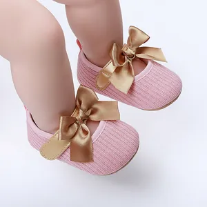 Detalle de zapatos de princesa tejidos en rosa para bebé con un gran lazo dorado