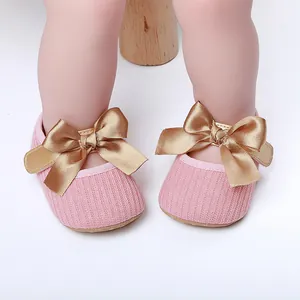 Detalle de zapatos de princesa rosa para bebé con un gran lazo de satén dorado decorativo.