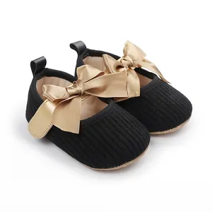 Detalle de zapatos de princesa para bebé en tela negra con elegantes lazos grandes de cinta dorada.