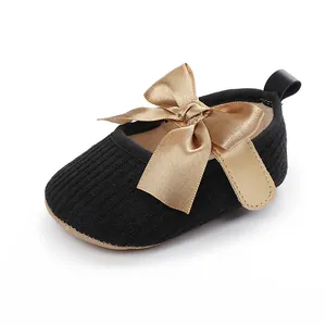 Detalle de zapato de princesa para bebé en tejido acanalado negro con gran lazo de satén dorado