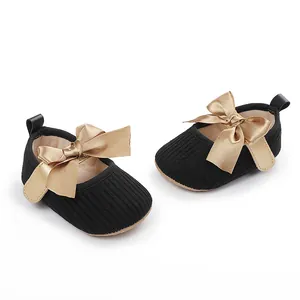 Primer plano de zapatos negros para bebé con elegantes lazos de satén dorado decorativos.