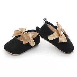 Detalle de zapatos de princesa para bebé negros con elegantes lazos de raso dorados.