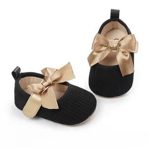 Detalle de zapatos de princesa para bebé negros con un gran lazo de satén dorado.