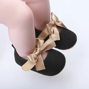 Detalle macro de zapatos de princesa para bebé negros con lazos de satén dorados.