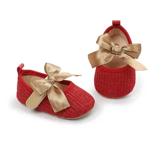 Vista detallada de zapatos de princesa para bebé en rojo con un gran lazo dorado decorativo.