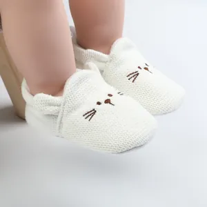 Detail view of white knitted baby walking shoes with cute cat embroidery