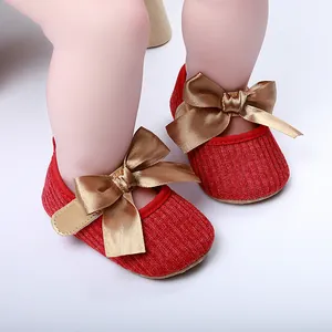 Primer plano de zapatos de princesa tejidos rojos para bebé con elegantes lazos de satén dorados