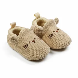 Close-up of beige knitted baby shoes with cute cat face embroidery and soft sole design.