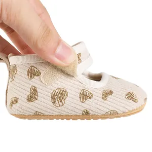 Detail shot of beige baby princess shoe with heart patterns and Velcro strap closure.