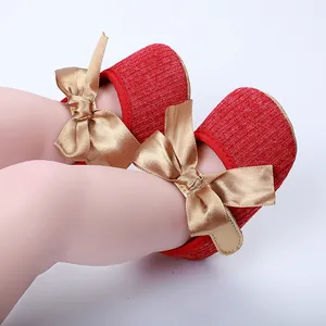 Primer plano de elegantes zapatos de princesa rojos para bebé con lazos de raso dorado