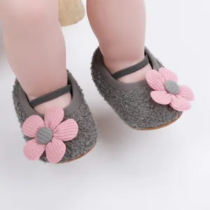 Nahaufnahme von grauen Plüsch-Babyschuhen mit dekorativer rosa Blume und weicher Sohle