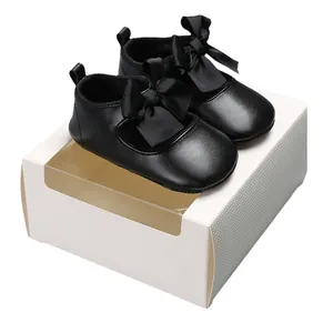 Elegantes zapatos de princesa para bebé negros con suela blanda y lazos sobre una caja de regalo