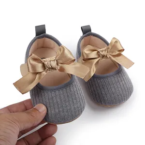 Vista detallada de zapatos de punto grises para bebé con elegantes lazos de raso dorado