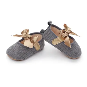 Detalle de zapatos de punto grises para bebé con elegantes lazos de satén dorado