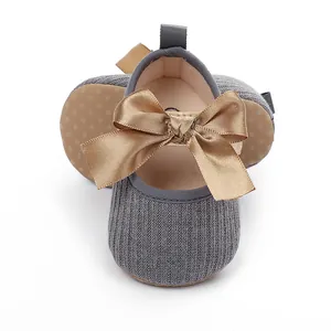 Detalle de zapatos de princesa de punto gris para bebé con un gran lazo de satén dorado