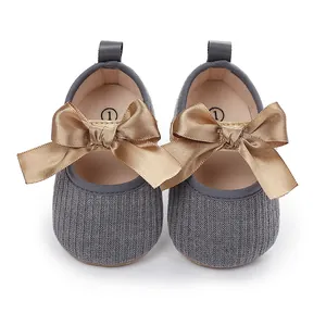 Detalle de zapatos de princesa grises para bebé con un gran lazo de raso dorado